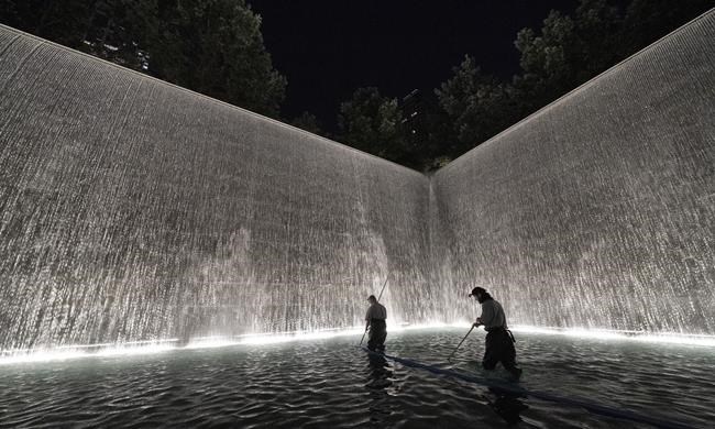 James Maroon, left, cleans the bottom of the south pool of the 9/11 Memorial with a vacuum, Wednesday, Aug. 4, 2021 in New York. On Sept. 11, 2001 he was going to work at the New York Mercantile Exchange, just west of the twin towers.
