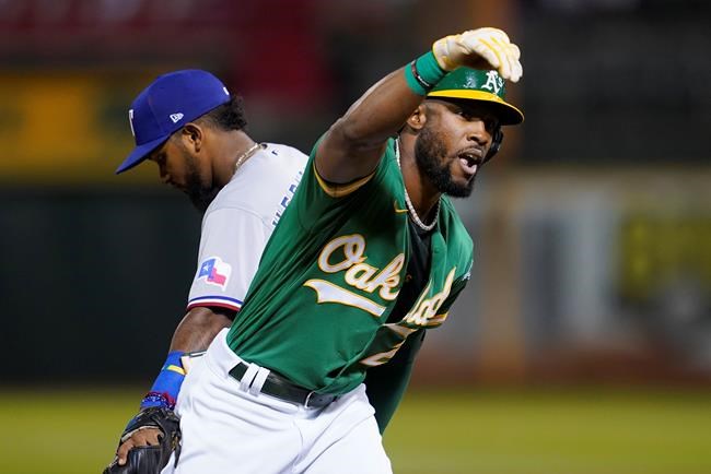 Oakland Athletics' Starling Marte gestures toward teammates after hitting an RBI triple, next to Texas Rangers' Yonny Hernandez during the fourth inning of a baseball game in Oakland, Calif., Friday, Sept. 10, 2021. (AP Photo/Jeff Chiu)