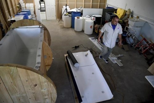 In this Wednesday, Aug. 11, 2021, photo, Chris Olachia walks past a nearly completed human body composting vessel in Arvada, Colo. On Sept. 7, Colorado became the second state after Washington to allow human body composting, and Oregon will allow the practice beginning next July. The vessel will be packed with wood chips and straw and will be able to compost a body in six months. About the size of a standard grave, the rectangular insulated wooden box is lined with waterproof roofing material and packed with wood chips and straw. Two large spool wheels on either end allow it to be rolled across the floor, providing the oxygenation, agitation and absorption required for a body to compost. (AP Photo/Thomas Peipert)