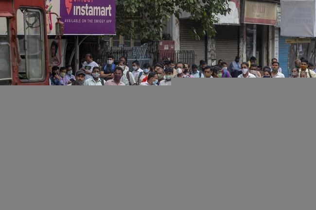 People wearing face masks as a precaution against the coronavirus wait at a bus stop in Mumbai, India, Monday, Sept. 27, 2021. (AP Photo/Rafiq Maqbool)