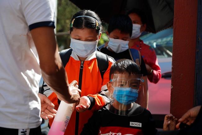 A door man gives hand sanitizer as Nepalese children arrive at their school that reopened after being closed for months due to the COVID-19 pandemic in Kathmandu, Nepal, Monday, Sept. 27, 2021. (AP Photo/Niranjan Shrestha)
