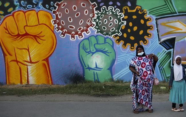 A woman and child stand next to an information mural telling people to fight the spread of the coronavirus, on a street in Mombasa, Kenya Monday, Sept. 27, 2021. (AP Photo/Brian Inganga)