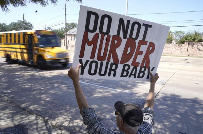 David Trujillo holds a sign as a school bus drives by on the street in front of a building housing an abortion provider in Dallas, Thursday, Oct. 7, 2021. A federal judge has ordered Texas to suspend a new law that has banned most abortions in the state since September. The order Wednesday by U.S. District Judge Robert Pitman freezes for now the strict abortion law known as Senate Bill 8. (AP Photo/LM Otero)