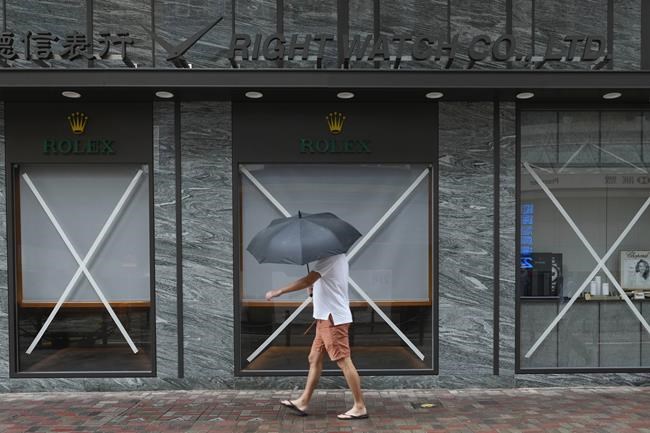 A man walks past a taped shop at an empty street as Typhoon Kompasu passes in Hong Kong Wednesday, Oct. 13, 2021. Hong Kong suspended classes, stock market trading and government services as the typhoon passed south of the city Wednesday. (AP Photo/Vincent Yu)