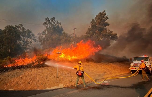 In this photo provided by the Santa Barbara County Fire Department, Cal firefighters extinguish a roadside fire off Calle Real near Refugio Rd., in Goleta, Calif., on Tuesday, Oct. 12, 2021. (Mike Eliason/Santa Barbara County Fire Department via AP)