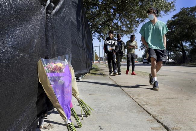 Flowers lie against the south fence surrounding the Astroworld festival grounds as festival attendants, from left, Andrew Diaz, Brandon Beauval, Joshua Robinson and Billy Nasser walk by the day after several people died and scores were injured during a concert the night before at NRG Park, Saturday, Nov. 6, 2021, in Houston. (AP Photo/Michael Wyke)