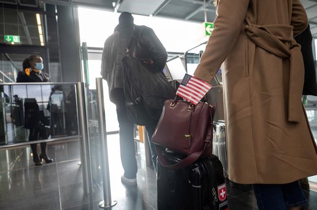 A woman walks through the boarding area at Frankfurt airport with a USA flag for a Lufthansa flight to New Yor, Frankfurt, Germany, Monday, Nov. 8, 2021. As of November 8, flights with vaccinated EU citizens to the USA will be allowed again. (Sebastian Gollnow/dpa via AP)