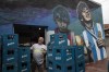 A worker laughs while loading crates onto a truck next to a mural depicting the late soccer star Diego Maradona outside the 