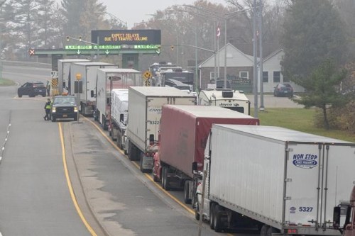 Transport trucks sit idling on Thousand Island Parkway at the toll waiting to cross into the US after its border opened up to non-essential travel in Lansdowne, Ontario, on November 8, 2021. THE CANADIAN PRESS/Lars Hagberg