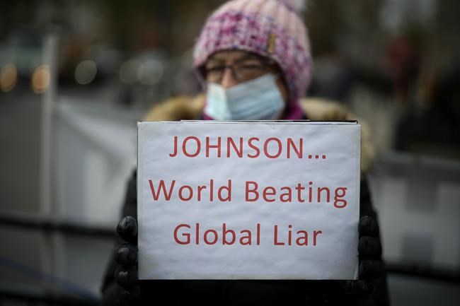 An anti-Boris Johnson protester holds a placard on the edge of Parliament Square across the street from the Houses of Parliament, in London, Wednesday, Dec. 8, 2021. British Prime Minister Boris Johnson on Wednesday ordered an inquiry and said he was
