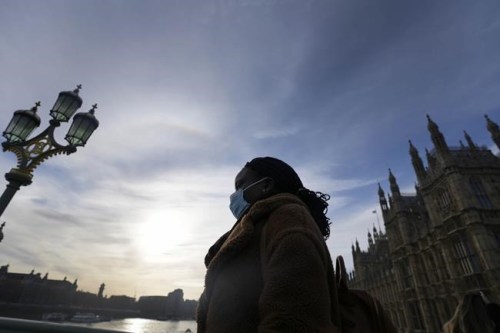 A woman wears a face covering as she crosses Westminster Bridge in London, Thursday, Dec. 9, 2021. British Prime Minister Boris Johnson has announced tighter restrictions to stem the spread of the omicron variant. He is again urging people to work from home and mandating COVID-19 passes to get into nightclubs and large events. (AP Photo/Frank Augstein)