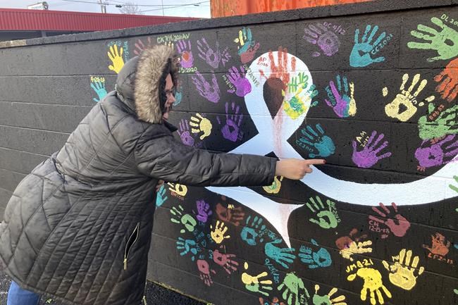 Anne Muilenburg, the office manager of Provoking Hope, an addiction recovery center in McMinnville, Ore., points to her handprint on the facility's parking lot wall on Thursday, Dec. 9, 2021. The wall has handprints of recovering addicts and the dates they became
