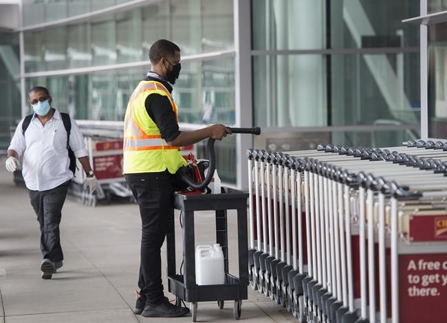 A man uses a sanitizer spray to wash down luggage carts at Toronto's Pearson International Airport in Toronto on Tuesday, June 23, 2020. Prime Minister Justin Trudeau says people will have to be careful as they finalize their Christmas plans this year, now that the highly transmissible Omicron variant is spreading through Canada. THE CANADIAN PRESS/Nathan Denette
