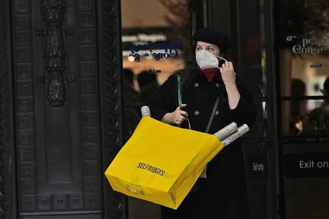 A woman takes off her face mask as she carries Selfridges bags after leaving the department store in London, Friday, Dec. 24, 2021. THE CANADIAN PRESS/AP/Alastair Grant