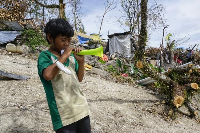 Romel Lo-ang plays with his horn, a Christmas gift from his godfather, near their damaged home due to Typhoon Rai in Cebu city, central Philippines on Christmas Day, Saturday, Dec. 25, 2021. His mother Alona Nacua said she and her husband managed to receive rice and four small cans of sardines and corned beef to be able to feed their family Saturday.