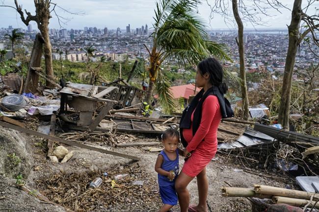 Alona Nacua, right, stands beside her son as she looks at their damaged house due to Typhoon Rai in Cebu city, central Philippines on Christmas Day, Saturday, Dec. 25, 2021. Nacua said she and her husband managed to receive rice and four small cans of sardines and corned beef to be able to feed their family Saturday.