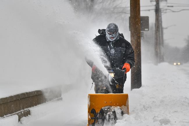Scott Sprecher uses a snow blower on a sidewalk Monday, Dec. 27, 2021, in St. Cloud, Minn. The city received between 3 and 4.5 inches of snow Sunday evening and Monday morning. More snow and cold are expected for this week. (Dave Schwarz/The St. Cloud Times via AP)