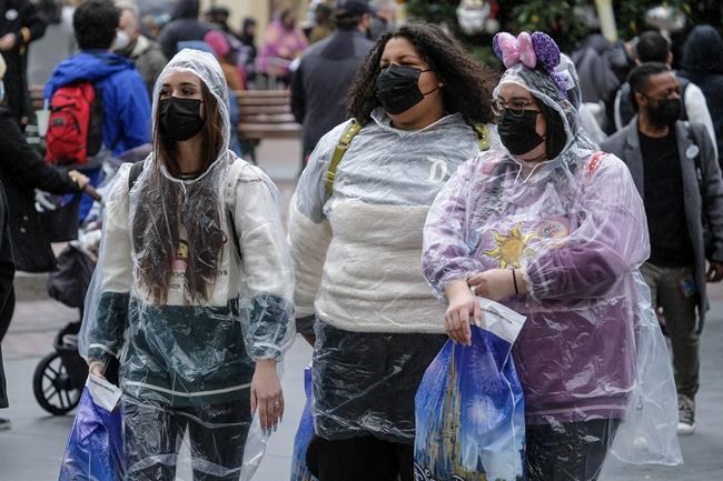 Visitors wearing rain coats and face masks walk down Main Street USA at Disneyland in Anaheim, Calif., Monday, Dec. 27, 2021. (AP Photo/Ringo H.W. Chiu)