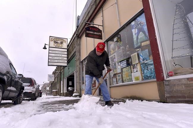 On a very cold morning V.F.W. Post 5878 member Bob Penrod clears the snow in front of the Tenino, Wash., post, Tuesday, Dec. 28, 2021, along with an adjacent beauty shop as winter weather strengthens its grip in the region. (Steve Bloom/The Olympian via AP)