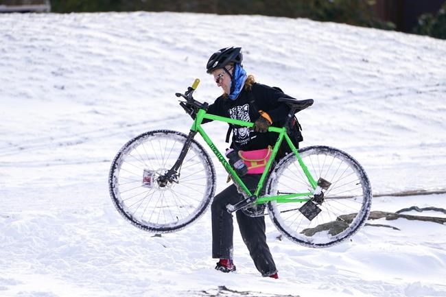 Apollo Leonard hefts his bike through snow too deep to ride in after stopping while out for a winter ride, Tuesday, Dec. 28, 2021, in Bellingham, Wash. Snow, ice and unseasonable cold in the Pacific Northwest and the Sierra Nevada are continuing to disrupt traffic, cause closures and force people to find refuge in emergency warming shelters. (AP Photo/Elaine Thompson)