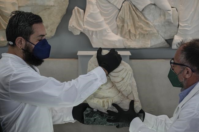 Two conservators hold a Parthenon fragment, on loan from the Antonino Salinas Regional Archaeological Museum of Palermo, at the Acropolis Museum, in Athens, on Monday, Jan. 10, 2022. The 2,500-year-old fragment is formally on loan from Sicily's A. Salinas Archaeological Museum, but both sides have said it could well end up permanently in Athens. Greek officials hope the move could encourage the British Museum to return its own extensive collection of sculptures from the Parthenon Temple on the Acropolis – a decades-old Greek demand that the London museum has so far rebuffed. (AP Photo/Thanassis Stavrakis)
