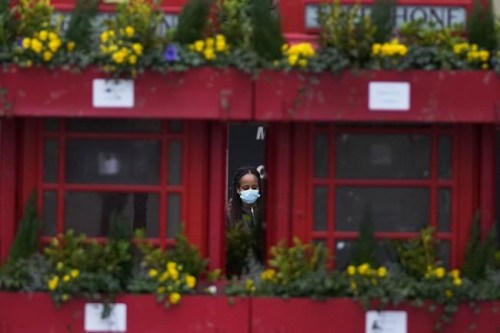 A woman wears a face mask as she walks past telephone boxes in Uxbridge, London, Monday, Jan. 10, 2022. (AP Photo/Frank Augstein)