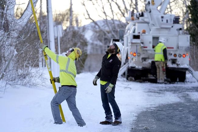 A lineman, left, uses a pole to untangle damaged power lines while working to restore electrical power, Sunday, Jan. 30, 2022, in Chatham, Mass. Gusty winds and falling temperatures are plunging the East Coast into a deep freeze as people dig out after a powerful nor'easter dumped mounds of snow, flooded coastlines and knocked out power to tens of thousands. (AP Photo/Steven Senne)