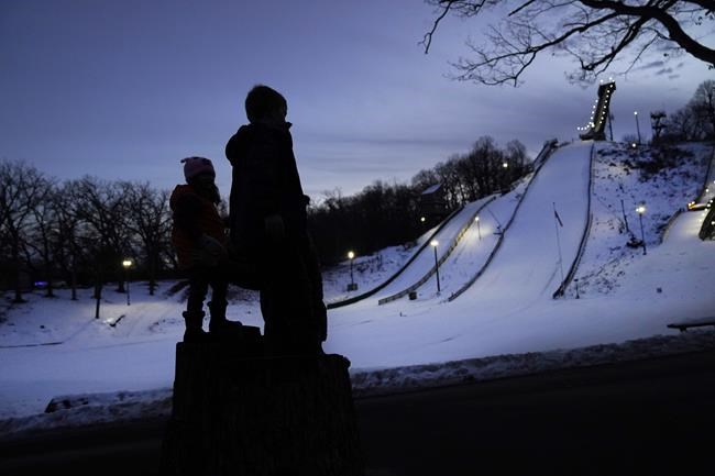 Julia Lindquist, 4, left, and Miles Stanton, 7, stand in silhouette on tree stumps and look over the five ski jump runs at the Norge Ski Club Tuesday, Jan. 18, 2022, in Fox River Grove, Ill. Lindquist was drawn to the sport when her parents would drive around the area for something safe to do during the COVID-19 pandemic last year. Each time the family of four drove near the club last year, the little girl in the back of the car told her parents of her hopes and dreams.