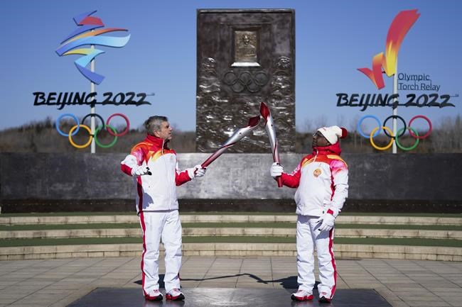 IOC President Thomas Bach, left, passes on the Olympic flame to Abdulla Shahid, President of UN General Assembly at the 2022 Winter Olympics, Friday, Feb. 4, 2022, in Beijing. (AP Photo/Jae C. Hong)