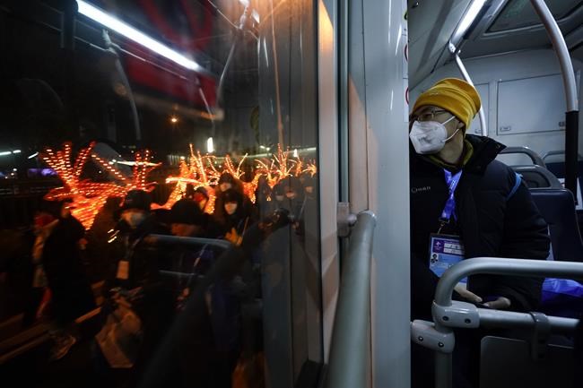 A journalist looks out the window of an Olympic shuttle bus as performers walk along the street with props used at the opening ceremony of the 2022 Winter Olympics, Saturday, Feb. 5, 2022, in Beijing. (AP Photo/Jae C. Hong)