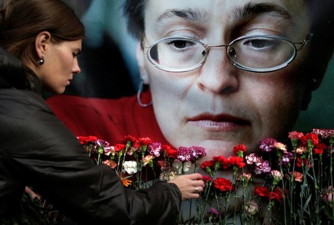 FILE- In this Oct. 7, 2009, file photo, a woman places flowers before a portrait of slain Russian journalist Anna Politkovskaya, in Moscow. Politkovskaya, who won international acclaim for her reporting on the human rights abuses in the Russian republic of Chechnya was shot dead in the elevator of her Moscow apartment building. (AP Photo/Pavel Golovkin, File)