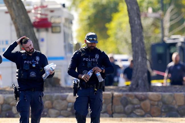 Police officers walk in the scene in front of a house where several Phoenix Police Department officers were shot and four others were injured after responding to a shooting inside the home Friday, Feb. 11, 2022, in Phoenix. The shooting suspect was found dead in the home following a barricade situation, and a woman at the home was critically injured. (AP Photo/Ross D. Franklin)