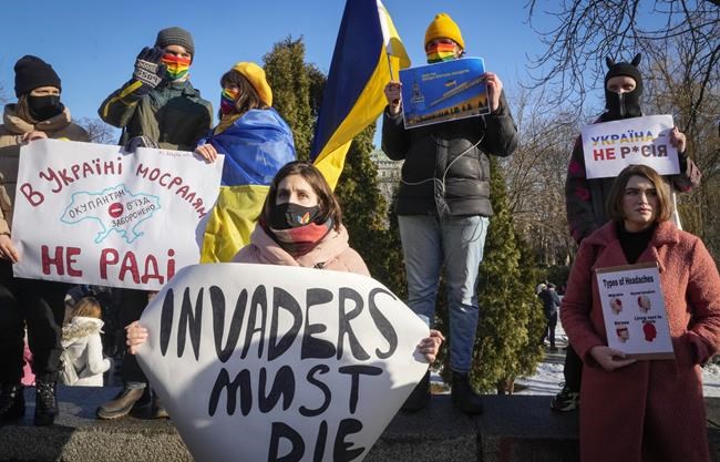 Ukrainian activists attend a rally in central Kyiv, Ukraine, Saturday, Feb. 12, 2022, during a protest against the potential escalation of the tension between Russia and Ukraine. Russian President Vladimir Putin and U.S. President Joe Biden are to hold a high-stakes telephone call on Saturday as tensions over a possibility imminent invasion of Ukraine escalated sharply and the U.S. announced plans to evacuate its embassy in the Ukrainian capital. Placard on left reads: