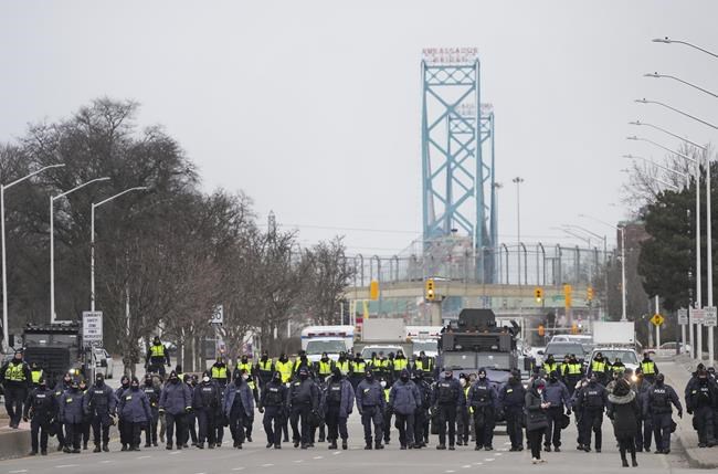 Police walk the line to remove all truckers and supporters after a court injunction gave police the power to enforce the law after protesters blocked the access leading from the Ambassador Bridge, linking Detroit and Windsor, as truckers and their supporters continue to protest against COVID-19 vaccine mandates and restrictions, in Windsor, Ont., Sunday, Feb. 13, 2022. The Canada Border Services Agency says the AmbassadorBridge border crossing between Windsor, Ont., and Detroit has reopened. THE CANADIAN PRESS/Nathan Denette