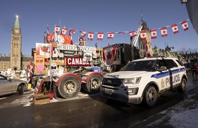 A police car passes trucks parked in front of the Parliament buildings, Tuesday, Feb. 15, 2022 in Ottawa. Figures behind the protests blockading Parliament Hill and different border crossing are championing new ways to finance their movement — including through their own token- as Ottawa invokes sweeping powers to crack down on their cash flow. THE CANADIAN PRESS/Adrian Wyld