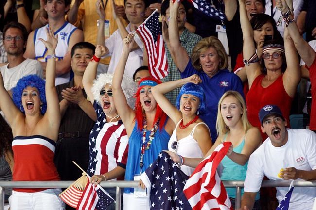 FILE - Fans cheer after a United States goal during their semifinal win over Serbia to advance to the gold medal match in the men's water polo at the Beijing 2008 Olympics in Beijing, Friday, Aug. 22, 2008. The Olympics are back in town 14 years later, but the atmosphere is much more subdued. Only a select few can watch the competitions in person because of the pandemic, and the 15,000 athletes, officials and others who have come for the Games have been kept completely separated from the population of Beijing. (AP Photo/Robert F. Bukaty, File)