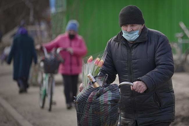 A man carries bags and a bunch of tulips on a bicycle in Stanytsia Luhanska, the only crossing point open daily, in the Luhansk region, eastern Ukraine, Tuesday, Feb. 22, 2022. Russian lawmakers on Tuesday authorized President Vladimir Putin to use military force outside the country — a move that could presage a broader attack on Ukraine after the U.S. said an invasion was already underway there. (AP Photo/Vadim Ghirda)