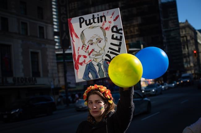 A woman holds a sign with a caricature of Russian President Vladimir Putin during a rally in support of the people of Ukraine in Vancouver, on Thursday, February 24, 2022. THE CANADIAN PRESS/Darryl Dyck