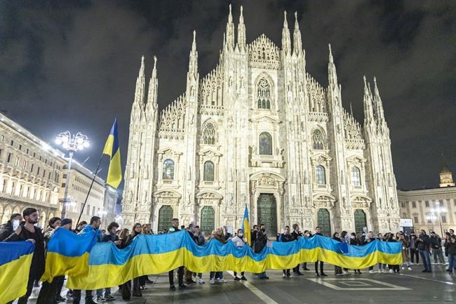 People hold a large flag of Ukraine in Duomo Square, Milan, Italy, Thursday Feb. 24, 2022. Russian President Vladimir Putin on Thursday announced a military operation in Ukraine and warned other countries that any attempt to interfere with the Russian action would lead to 'consequences you have never seen.' (LaPresse via AP)