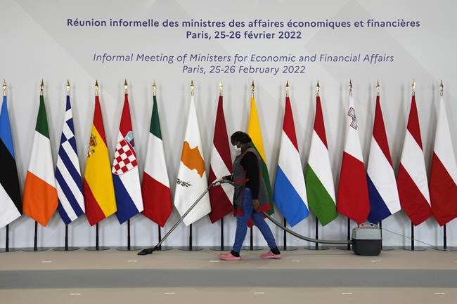 A woman hoovers the podium after the family picture during a European Finance Ministers meeting, Friday, Feb. 25, 2022 in Paris. The world has made it clear that a military intervention in Ukraine is off the books, so most countries on Friday were throwing ever more punishment at Moscow — from financial to football sanctions. (AP Photo/Francois Mori)