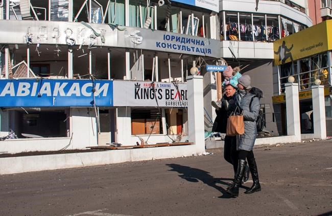 A couple with a child on the shoulders weals past a damaged by shelling building in Kharkiv, Ukraine, Tuesday, March 15, 2022. (AP Photo/Andrew Marienko)