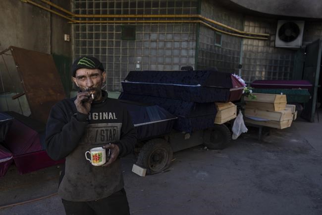 Worker Ruslan Trishchuk, 40, smokes a cigarette while taking a break outside the crematorium of Baikave cemetery in Kyiv, Ukraine, Monday, March 21, 2022. (AP Photo/Rodrigo Abd)