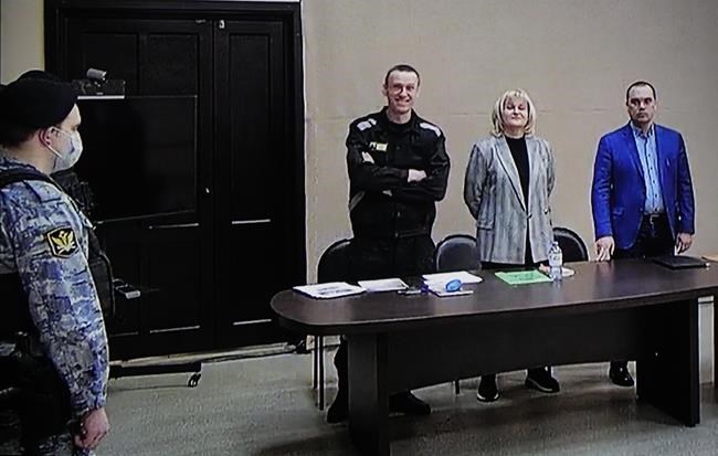 Russian opposition leader Alexei Navalny, centre, is seen via a video link provided by the Russian Federal Penitentiary Service, standing next to his layers during a court session in Pokrov, Vladimir region, about 100 kilometers (62 miles) east of Moscow, Russia, Tuesday, March 22, 2022. The Russian authorities are seeking a 13-year prison sentence for opposition leader Alexei Navalny in a trial Kremlin critics see as an attempt to keep President Vladimir Putin's most ardent foe in prison for as long as possible. (AP Photo/Alexander Zemlianichenko)