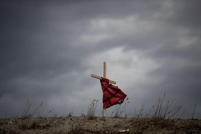 A child's dress hung on a cross blows in the wind near the former Kamloops Indian Residential School to honour 215 children whose remains have been discovered buried near the site in Kamloops, B.C., on Friday, June 4, 2021. The Catholic religious order that operated some residential schools in Canada says it will give researchers access to its archives in Rome. THE CANADIAN PRESS/Darryl Dyck