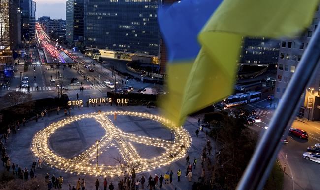 People stand around a giant peace sign with the message 'Stop Putin's Oil', put up by demonstrators ahead of an EU and NATO summit in Brussels, Tuesday, March 22, 2022. Protestors on Tuesday called on EU leaders to impose a full ban on Russian fuels and to hold one minute of silence to honor the victims of war. (AP Photo/Geert Vanden Wijngaert)