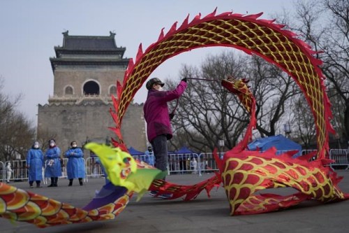Community workers wearing protective suits watch over a masked resident twirling a dragon shaped ribbon near a barricaded coronavirus testing site setup outside the Drum Tower, Wednesday, March 23, 2022, in Beijing, China. A fast-spreading variant known as 