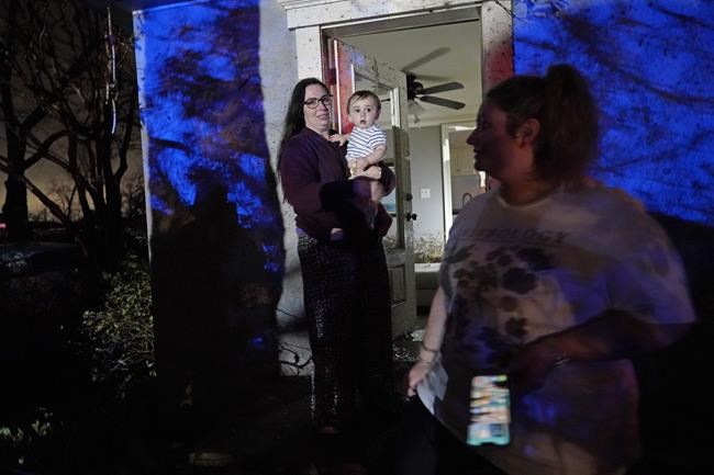 Annelise Cassar holds her nephew Eliam Cruice, 9 months, as mother Arianna Cruice, right, surveys damage around them after a tornado swept through the area in Arabi, La., Tuesday, March 22, 2022. A tornado tore through parts of New Orleans and its suburbs Tuesday night, ripping down power lines and scattering debris in a part of the city that had been heavily damaged by Hurricane Katrina 17 years ago. (AP Photo/Gerald Herbert)