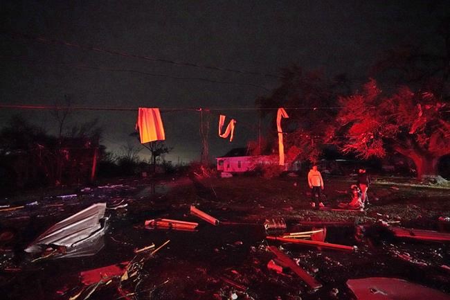Residents illuminated by fire truck lights stand amongst debris after a tornado swept through the area in Arabi, La., Tuesday, March 22, 2022. A tornado tore through parts of New Orleans and its suburbs Tuesday night, ripping down power lines and scattering debris in a part of the city that had been heavily damaged by Hurricane Katrina 17 years ago. (AP Photo/Gerald Herbert)