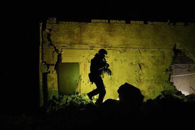 A Ukrainian special police officer walks next to a destroyed building as he patrols during night curfew in Kharkiv, Ukraine, Sunday, March 27, 2022. (AP Photo/Felipe Dana)