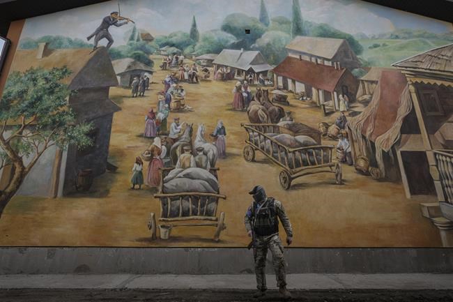 A member of the security team walks by a Fidler on the Roof themed mural at the Anatevka Jewish settlement outside Kyiv, Ukraine, Sunday, March 27, 2022. Anatevka was built in 2015 at the initiative of Rabbi Moshe Azman for Jewish people displaced by the conflict in eastern Ukraine and is still used for families who need to leave their homes in areas where affected by fighting between Russian and Ukrainian forces.(AP Photo/Vadim Ghirda)